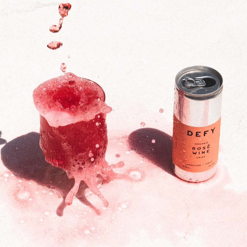 Can of DEFY Italian rosé wine next to a glass with the bright rosé wine splashing everywhere; vegan organic and delicious – eco-friendly.