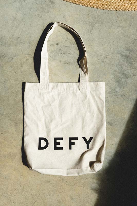 DEFY recycled cotton tote bag with the DEFY wordmark, on concrete..