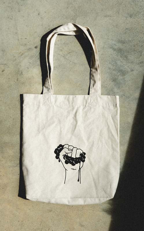 DEFY recycled cotton tote bag with the DEFY fist icon, on concrete.